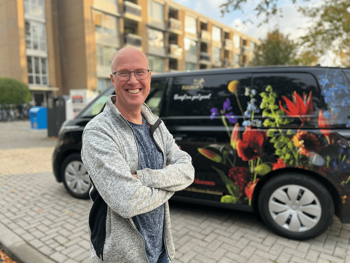 Sandor Verkerk voor zijn zwarte elektrische bestelbus met bloemen erop.