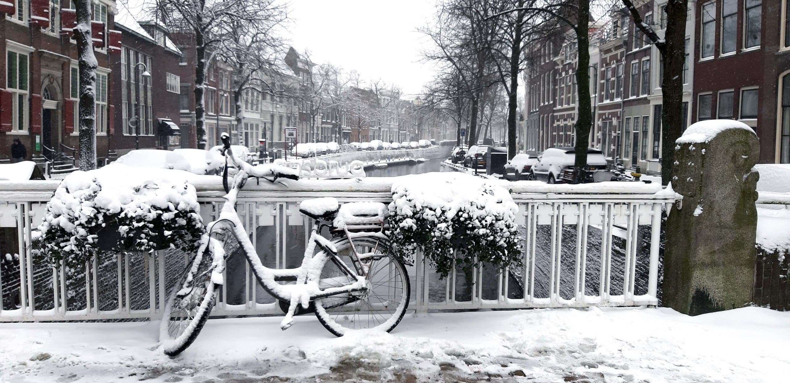 Op de foto staan de Westhaven en de Oosthaven, gefotografeerd vanaf de St. Jansbrug. Op de brug staat een fiets en er ligt een flinke laag sneeuw op straat, de brug en de fiets. 