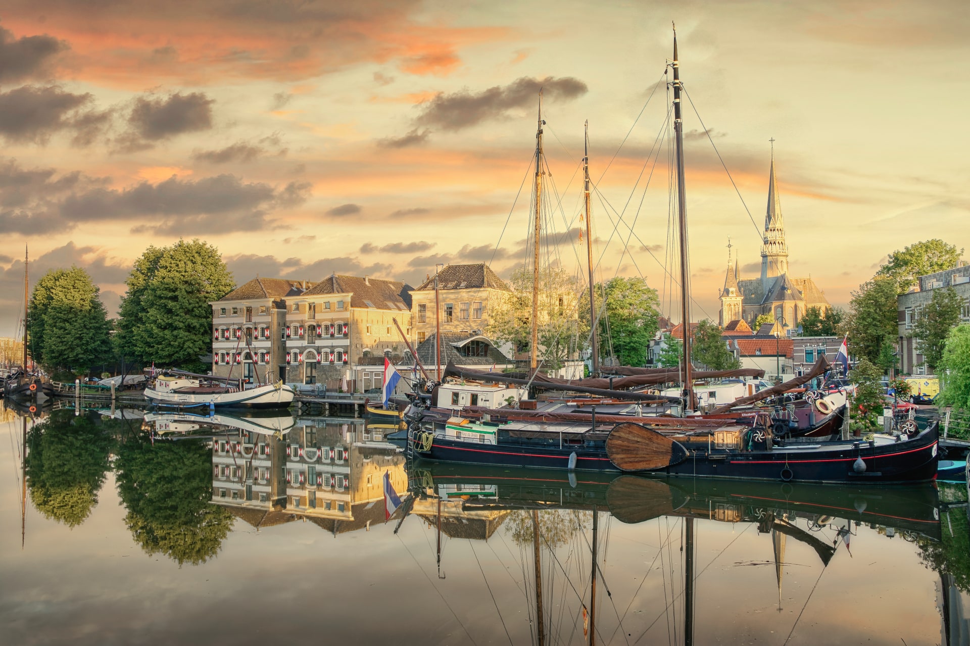 Op de foto staat de Museumhaven tijdens zonsondergang. Er zijn meerdere schepen te zien, die weerspiegelen in het water.